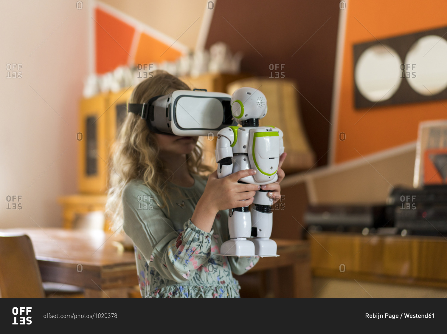 Girl with virtual reality simulator headset holding robot while playing in living room at home