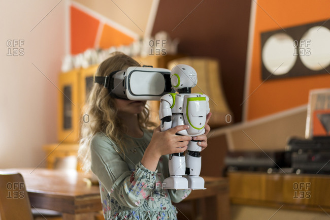 Girl with virtual reality simulator headset holding robot while playing in living room at home