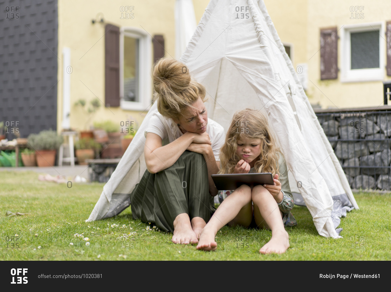Confused mother and daughter looking at digital tablet while sitting in tent on grass during weekend