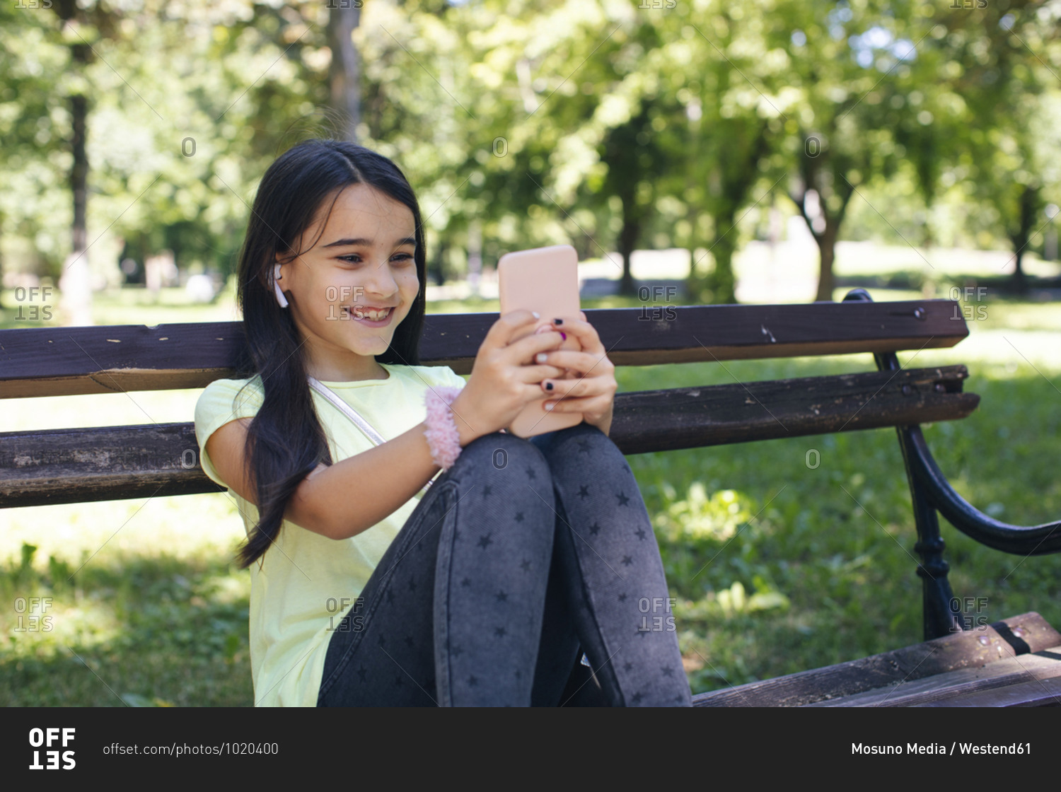 Smiling girl using phone while sitting on bench in park