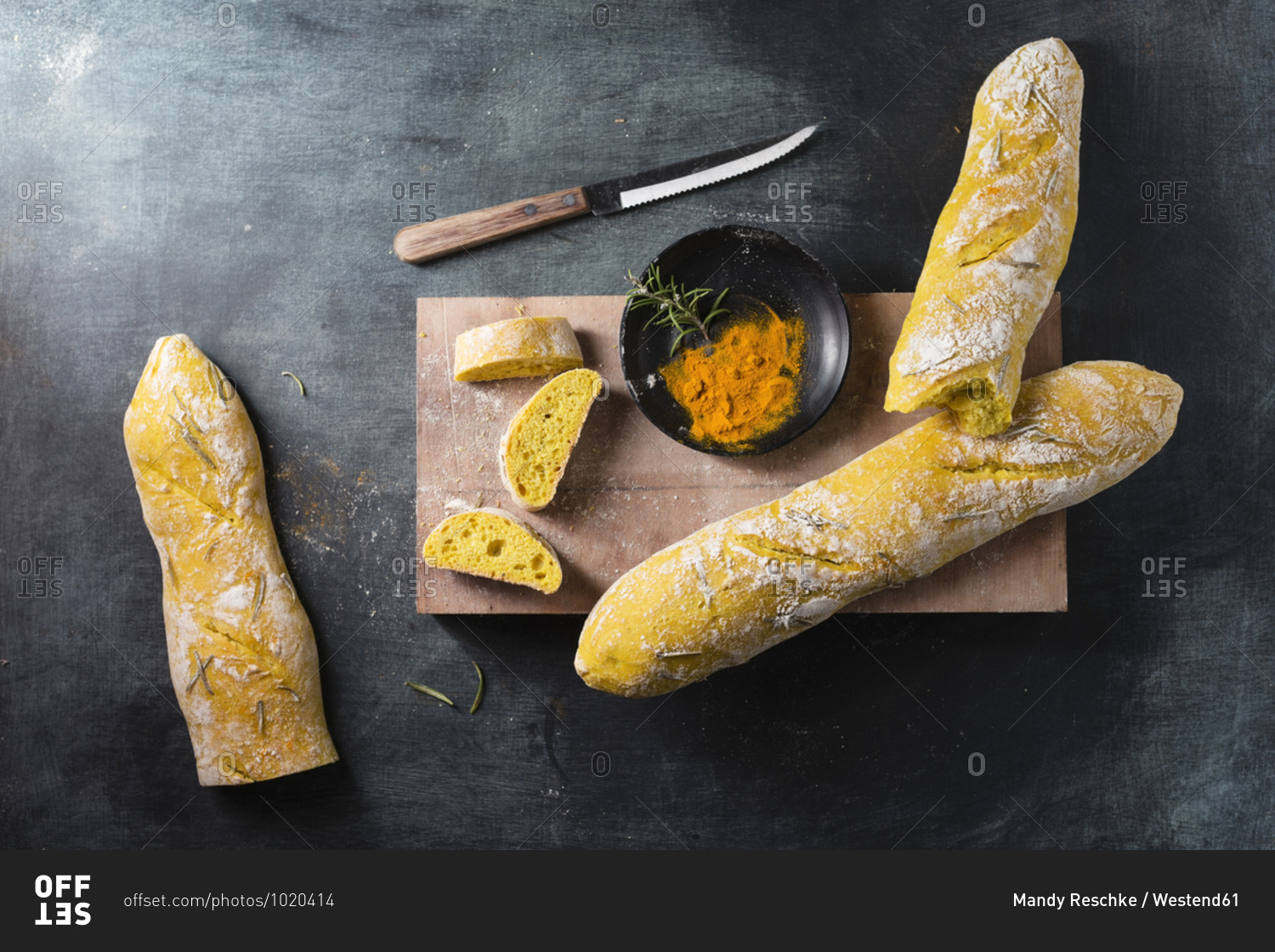 Cutting board- kitchen knife- fresh baguettes and bowl with turmeric and rosemary
