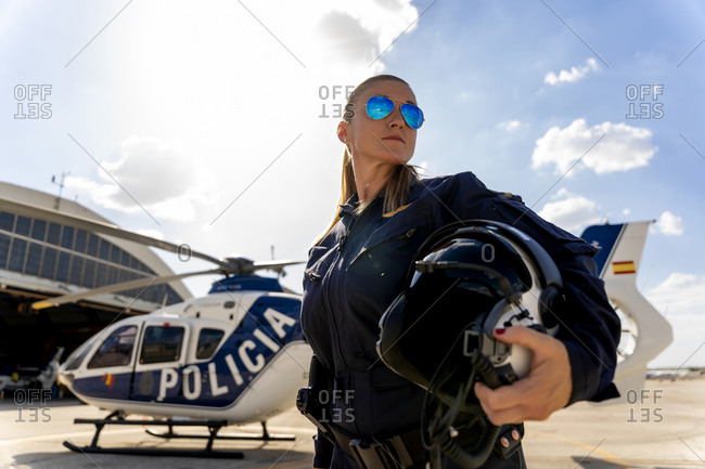 Confident female police pilot standing against sky on sunny day
