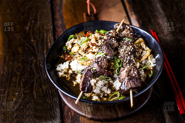 Bowl of ready-to-eat teriyaki rice with Chinese cabbage and grilled beef skewers