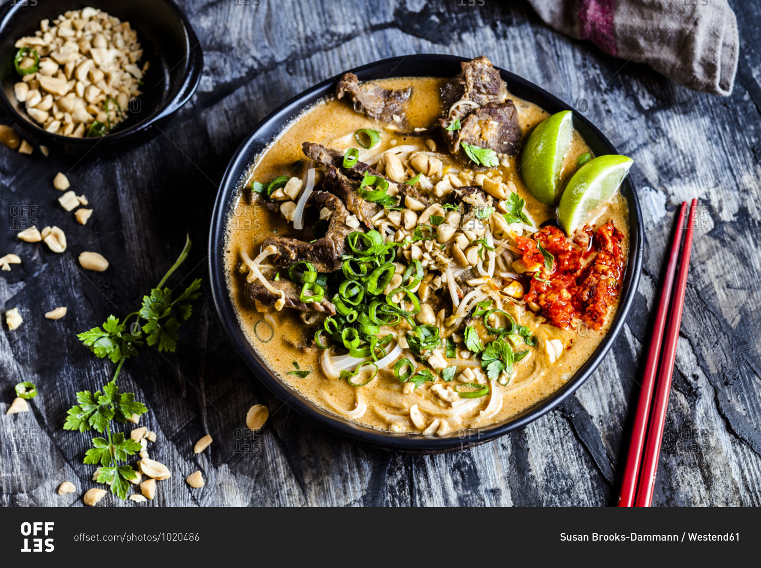 Bowl of red curry soup with rice noodles- beef- vegetables- scallion- peanuts and lime