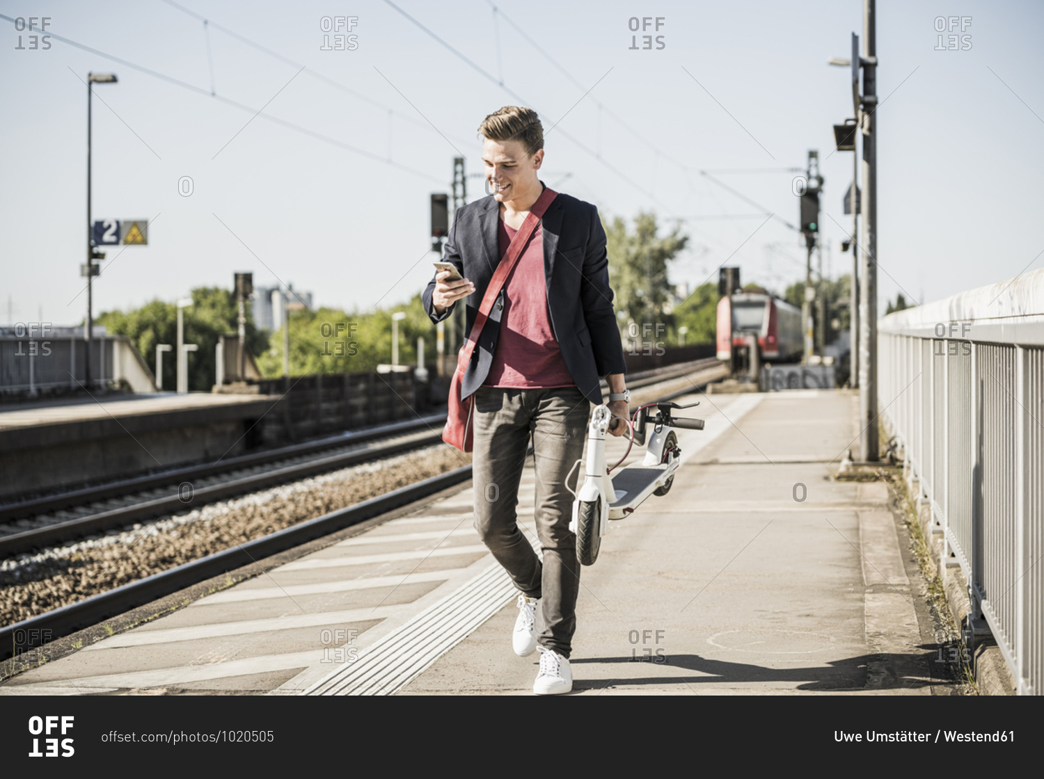 Man with push scooter using mobile phone while walking on railroad station platform