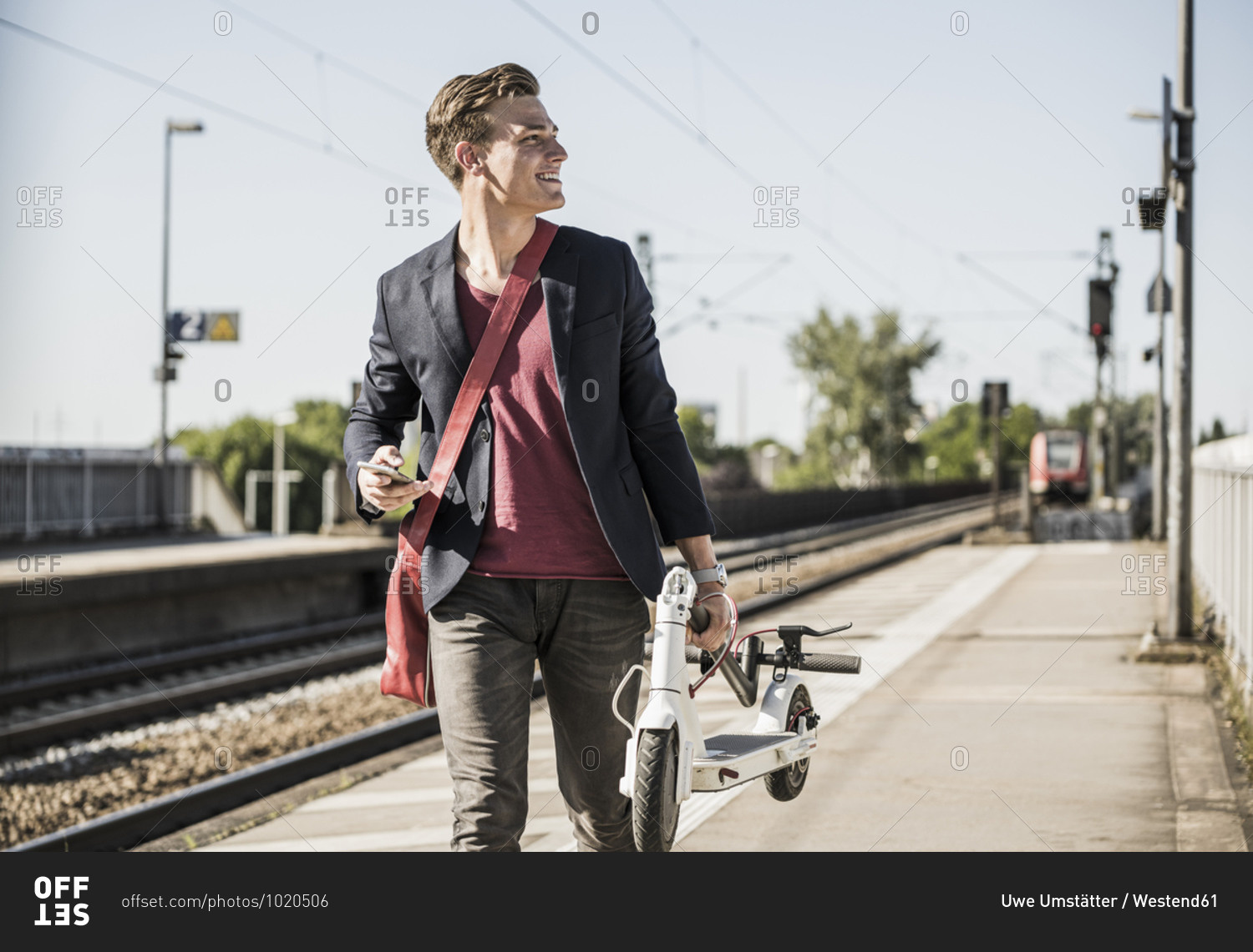 Smiling man with push scooter looking away while walking on railroad station platform