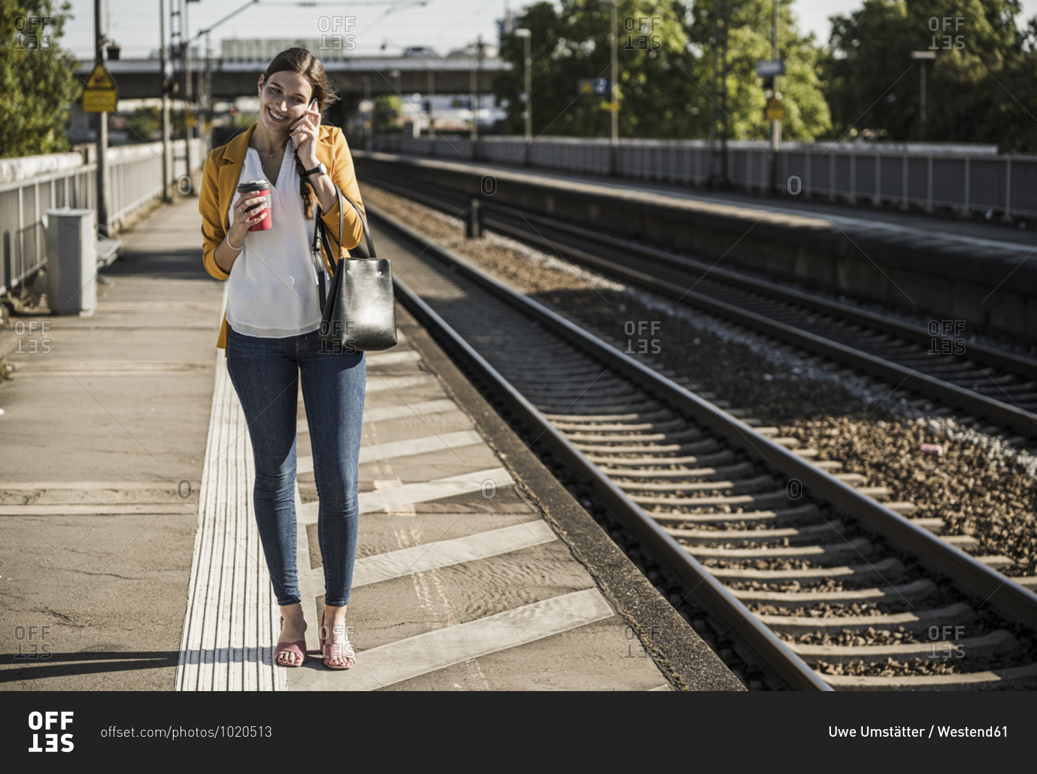 Smiling woman talking on mobile phone while standing on railroad station platform