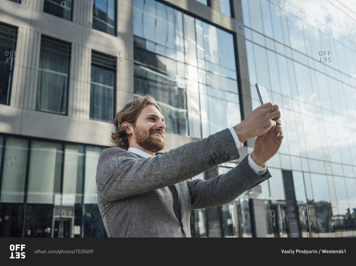 Smiling male professional taking selfie against office building at downtown district