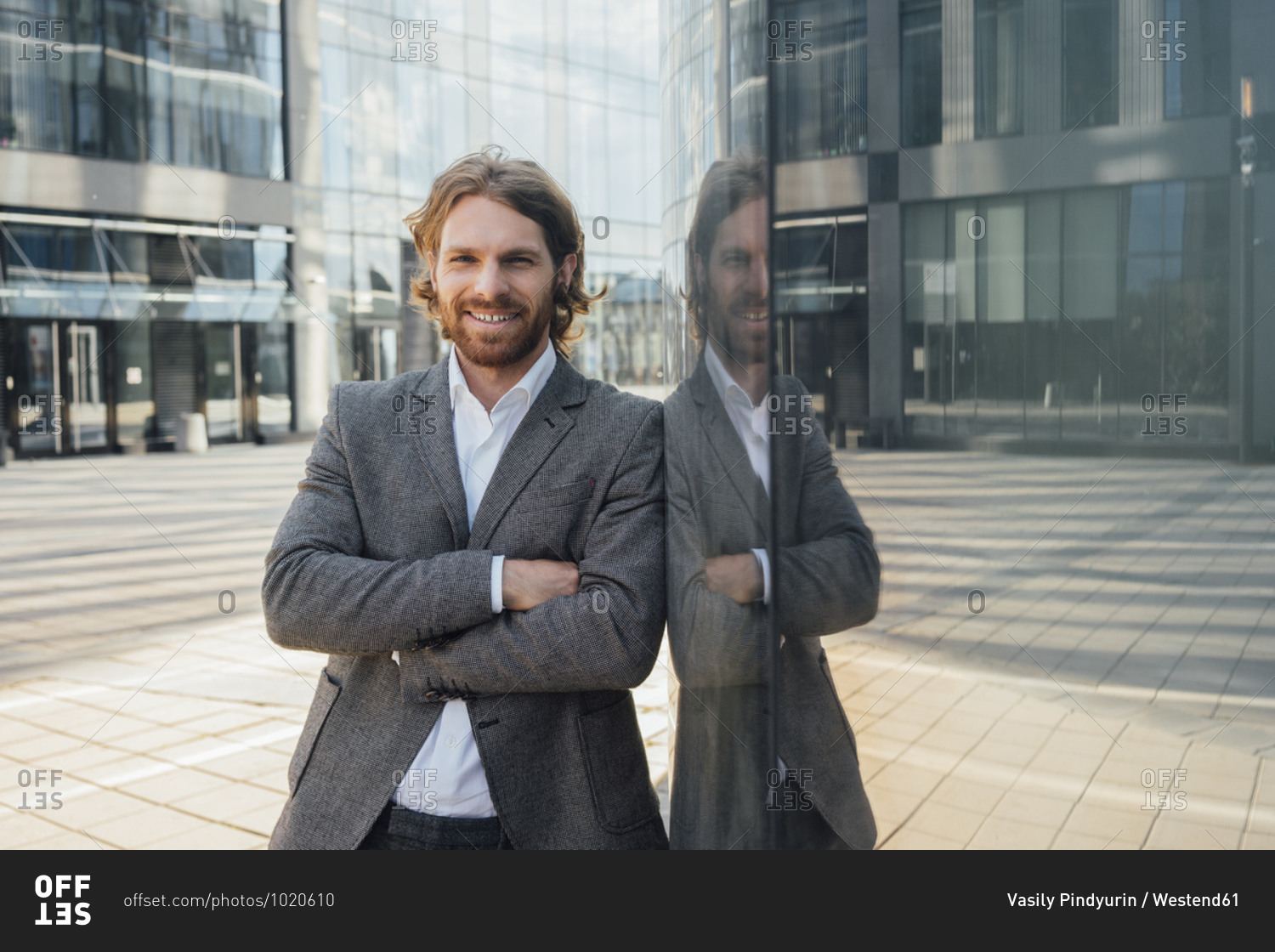 Handsome businessman standing with arms crossed by reflection on office building in financial district