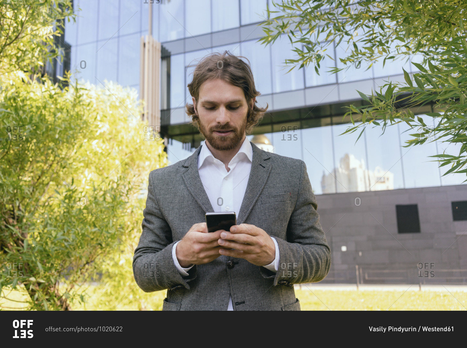 Beard handsome businessman using smart phone while standing against office building