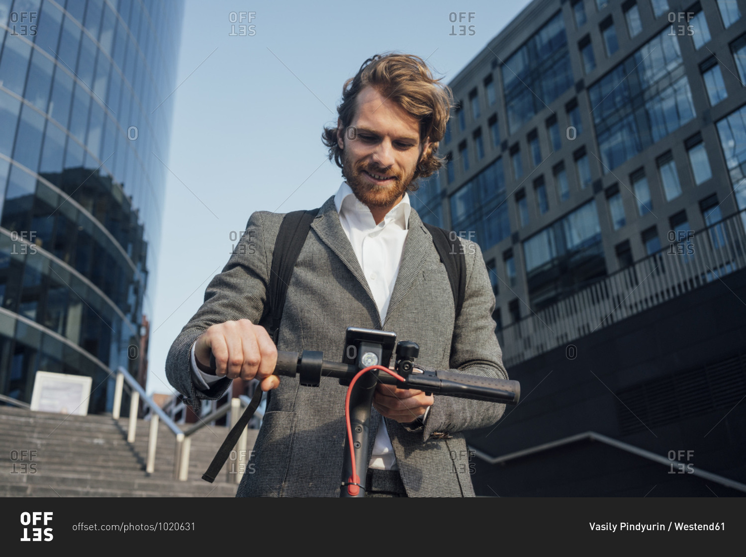 Male entrepreneur using mobile phone while standing with electric push scooter at downtown