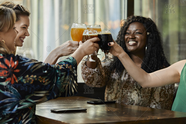 Happy female friends clinking craft beer glasses in a pub