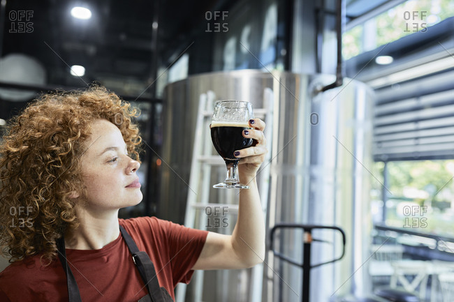 Woman working in craft brewery checking quality of a beer