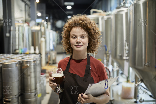 Portrait of confident woman holding clipboard and beer glass in craft brewery