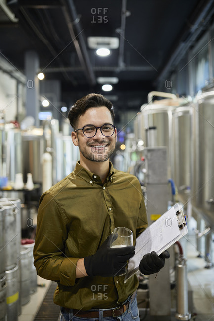 Portrait of happy man holding clipboard and beer glass in craft brewery
