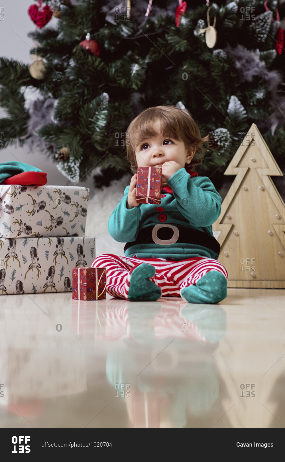 A little 12-month-old christmas elf with a christmas tree and gifts