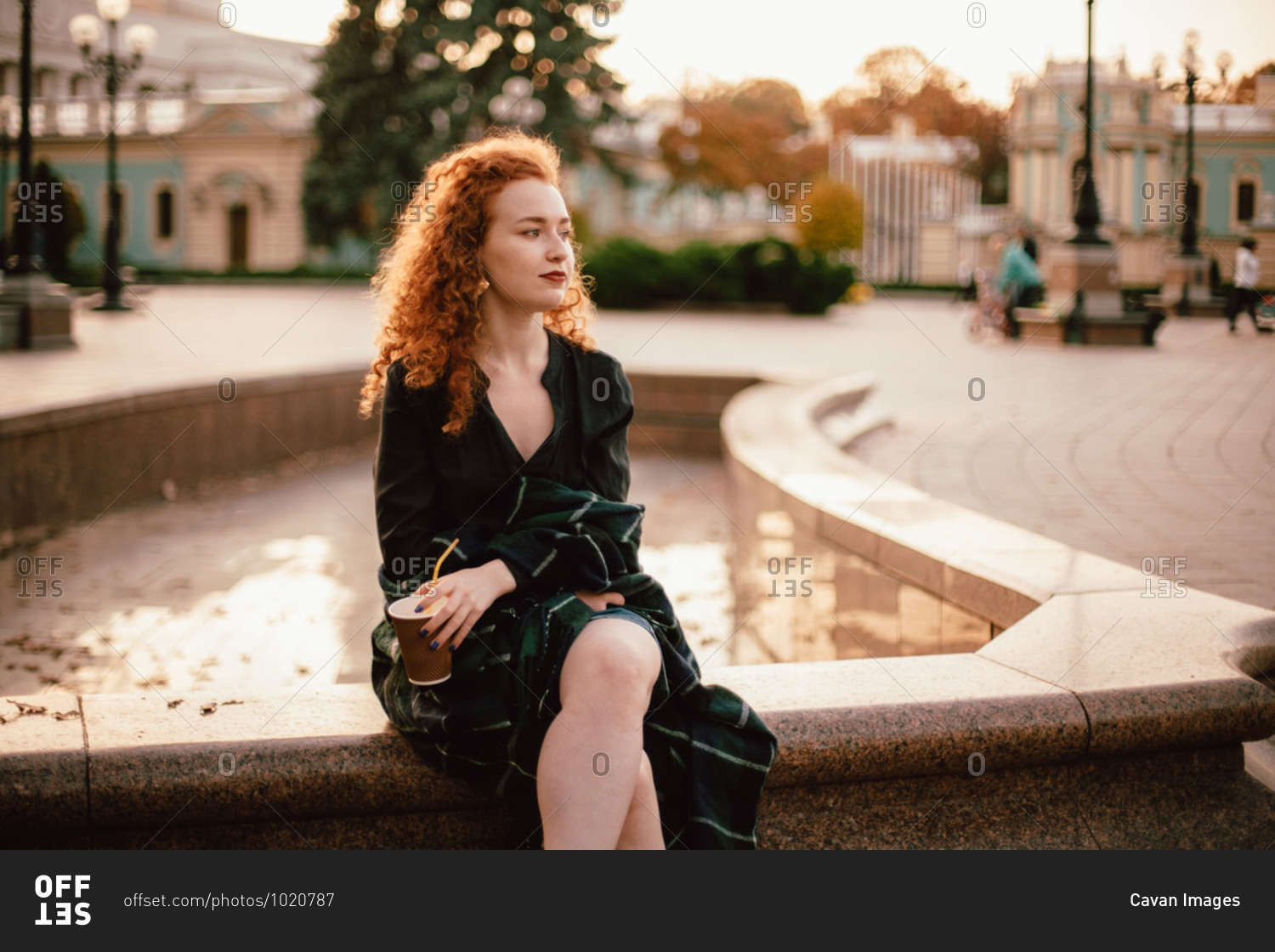 Young thoughtful red head woman sitting on fountain in city