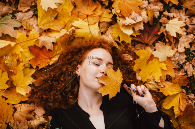 Young woman holding leaf lying in orange leaves in autumn park