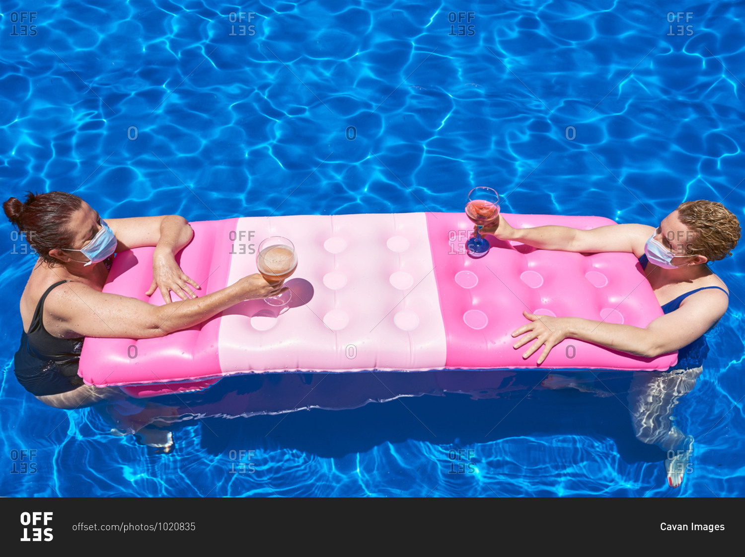 Two women bathe in a pool with a sanitary mask. they maintain the safety distance.