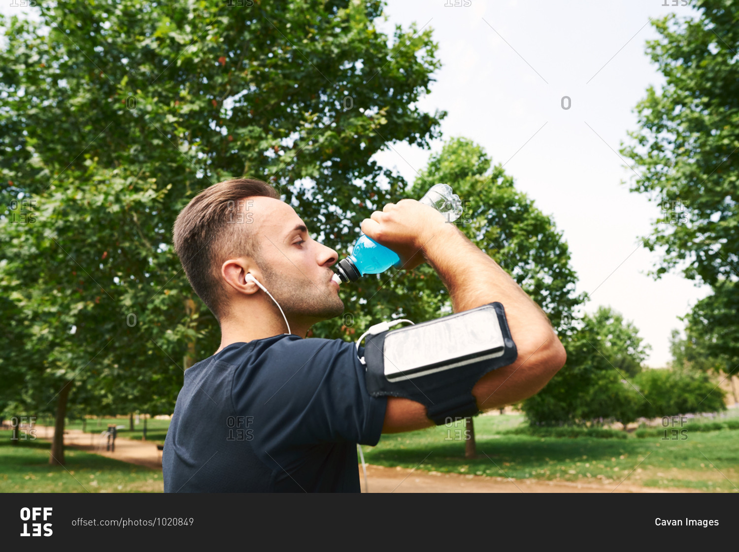 Man drinking sports drink after training. he is in an outdoor park.