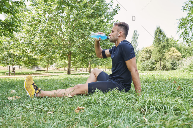 Man drinking sports drink after training. he is in an outdoor park.