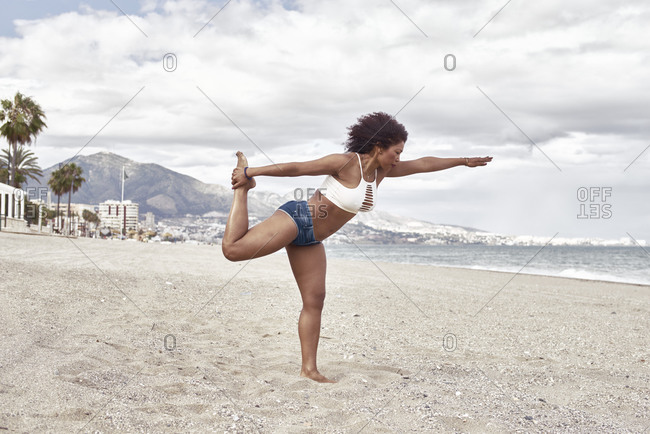 Black woman in short jeans poses on the beach balancing