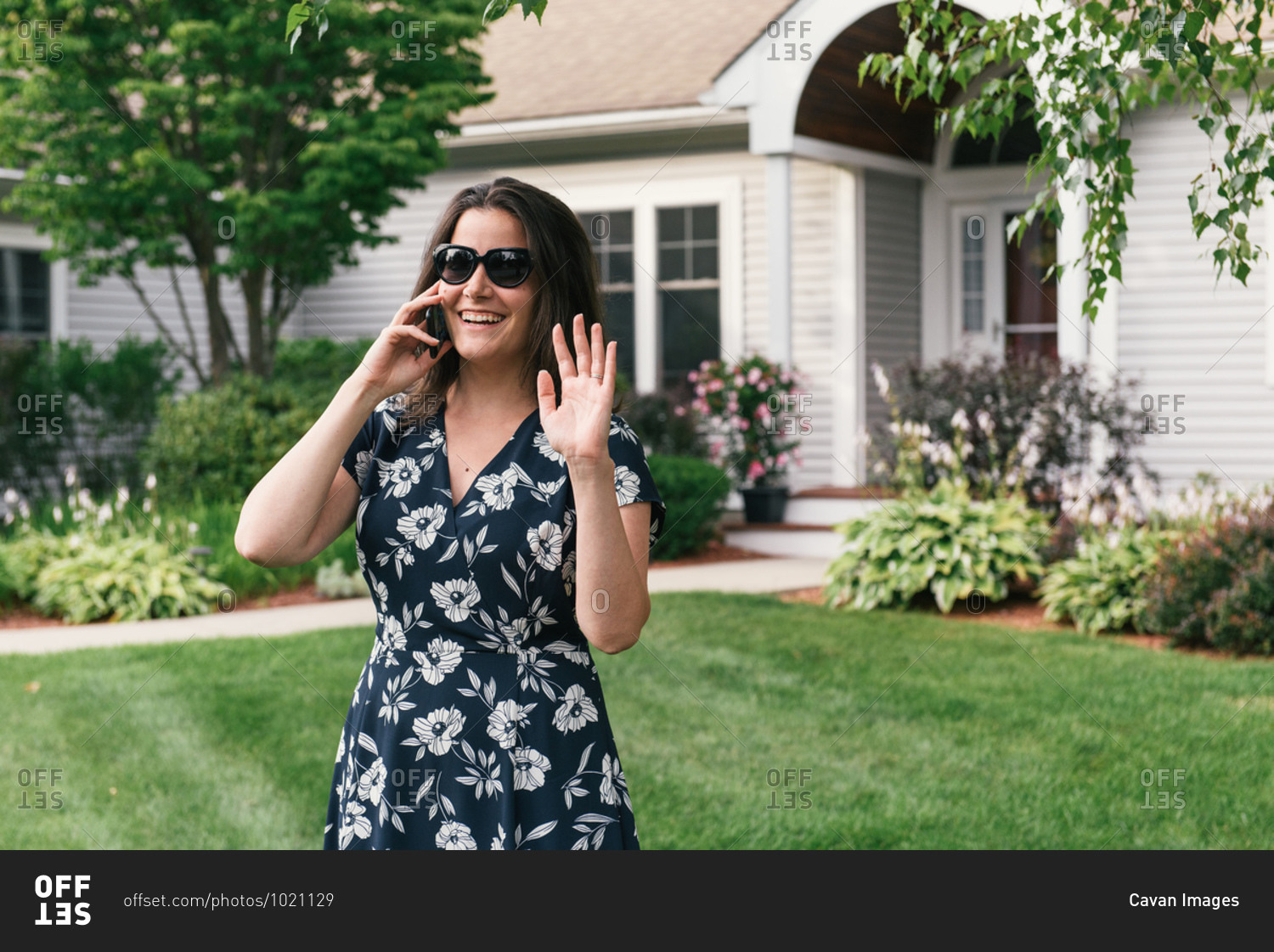 Woman on cell phone waving to neighbors in front of landscaped home