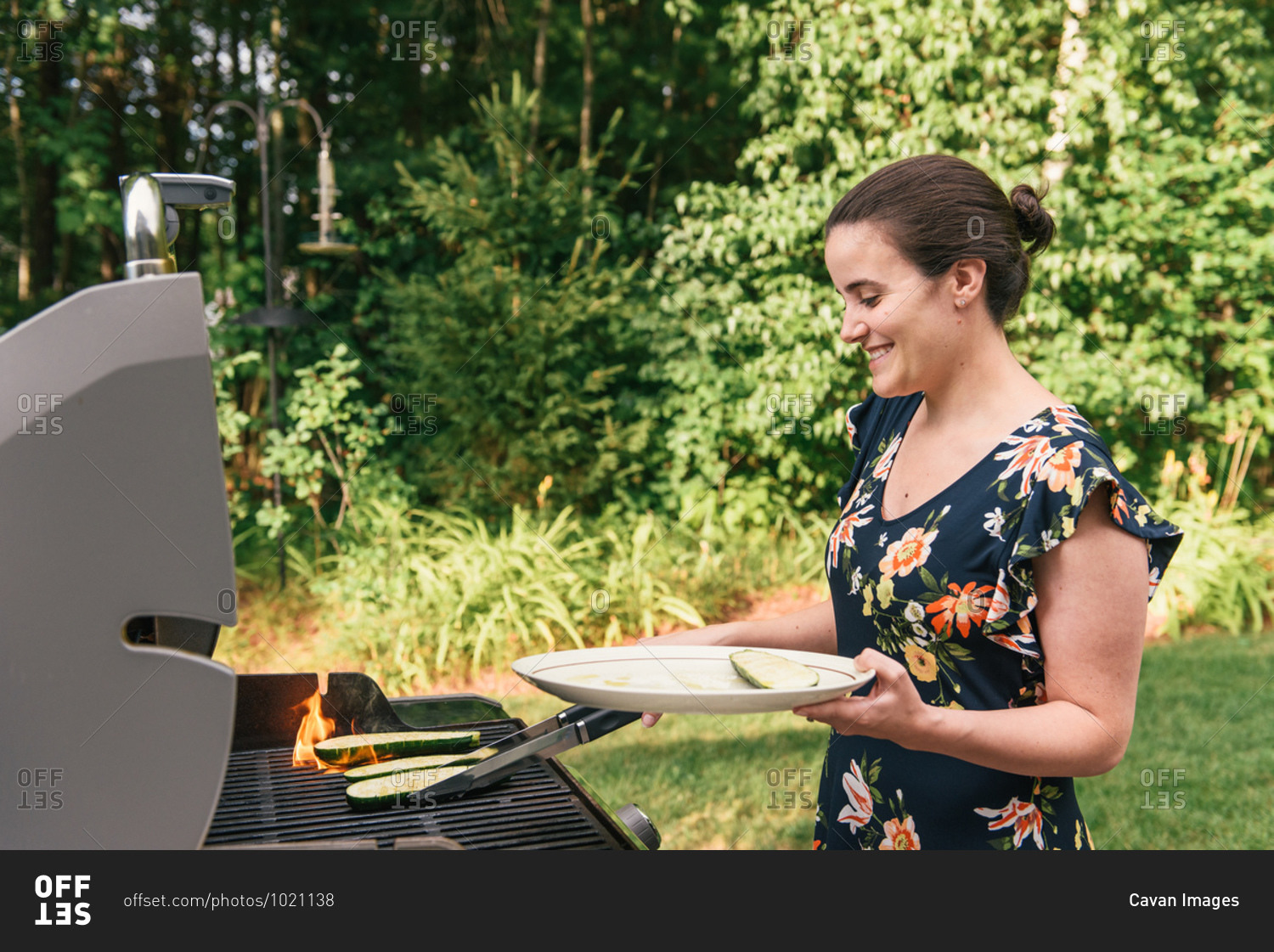 Woman grilling squash with flames on barbecue at home grill
