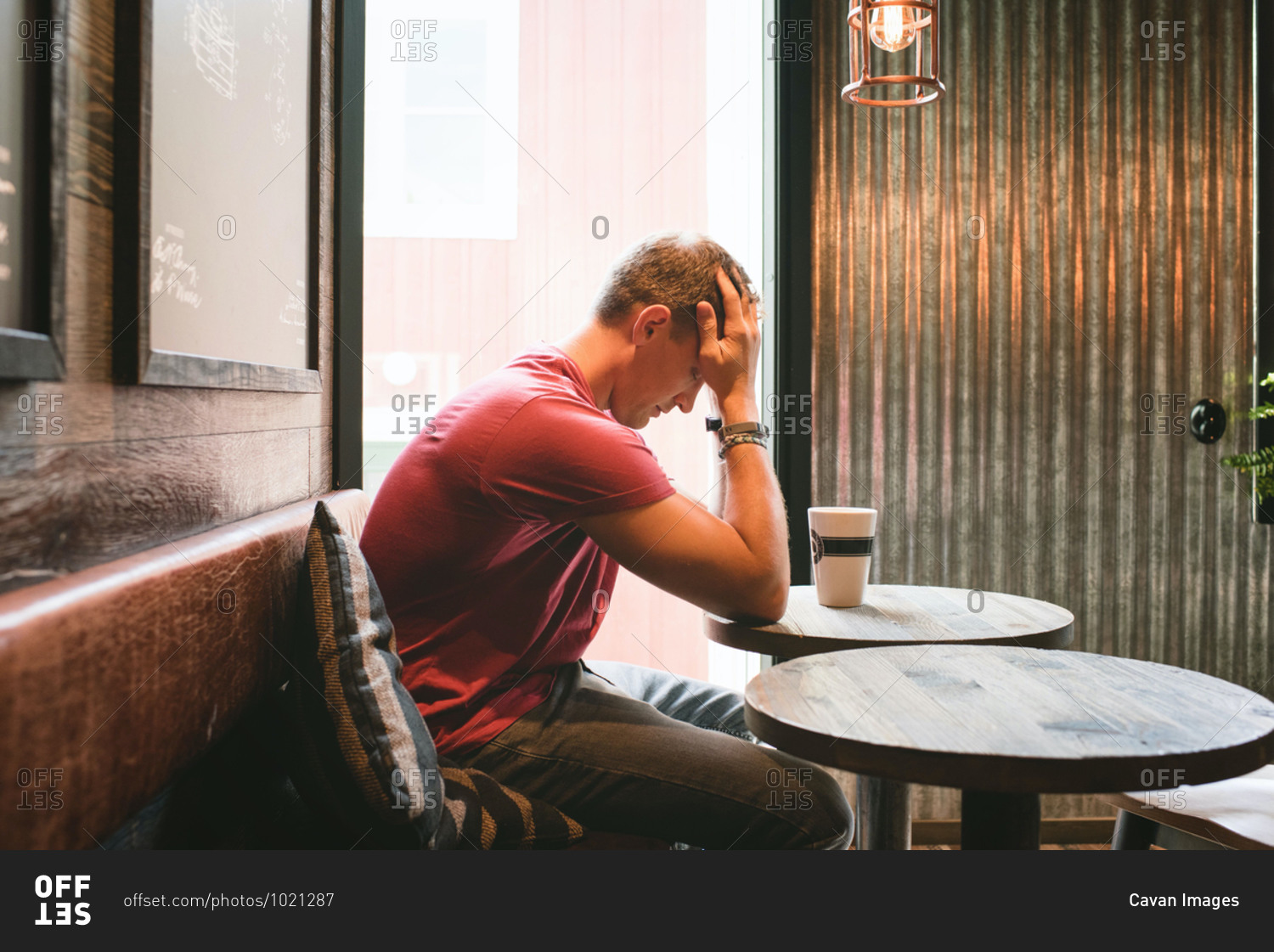 Man sat feeling stressed with his face in his hands in a cafe
