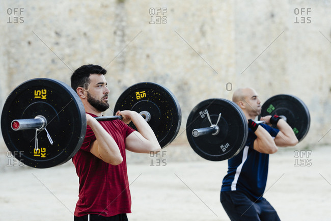 Two weightlifters lifting weights in an urban environment.