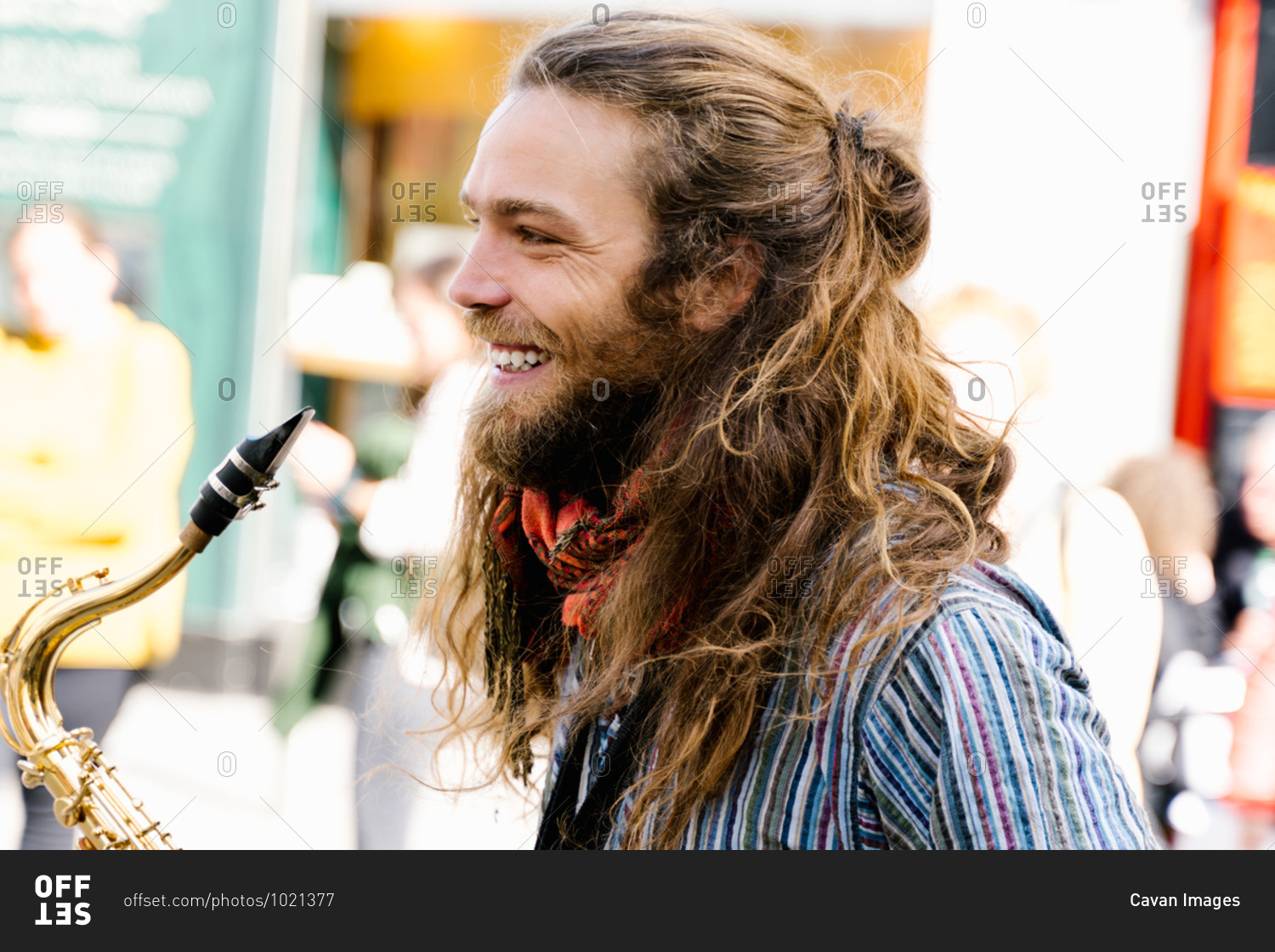 Portrait of a young man with long hair smiling with a saxophone in hands