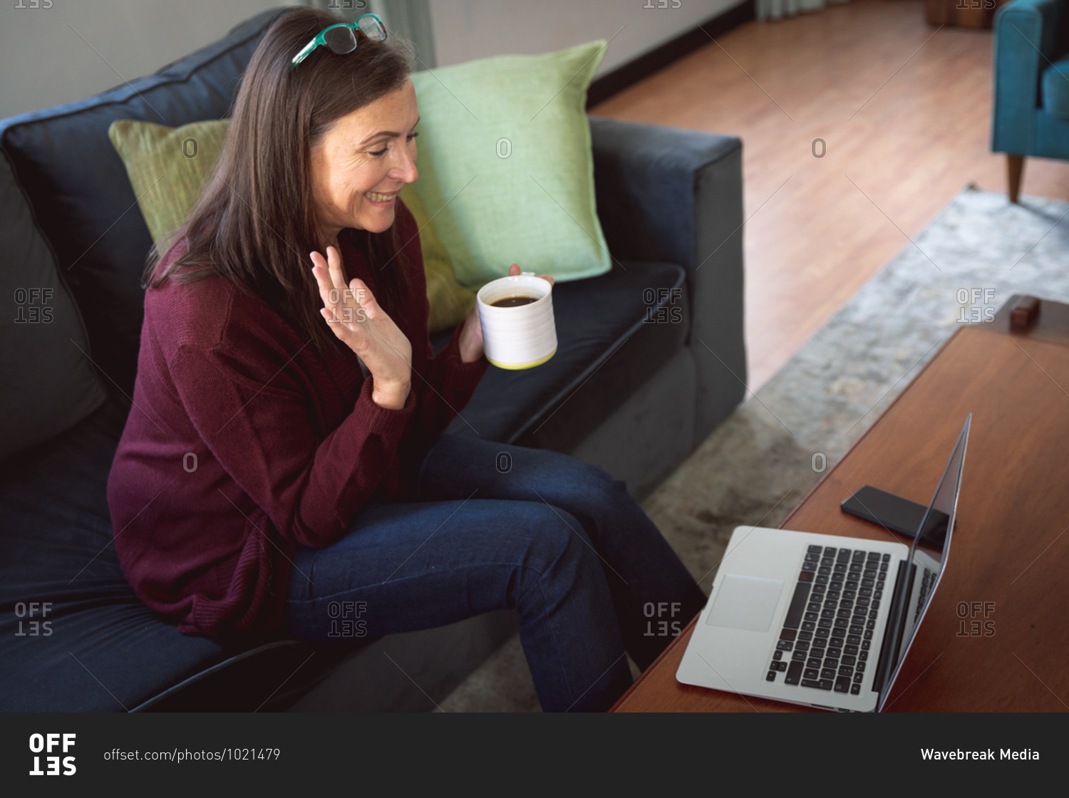 Caucasian woman enjoying time at home, social distancing and self isolation in quarantine lockdown, sitting on sofa in sitting room, using a laptop, waving during video call.