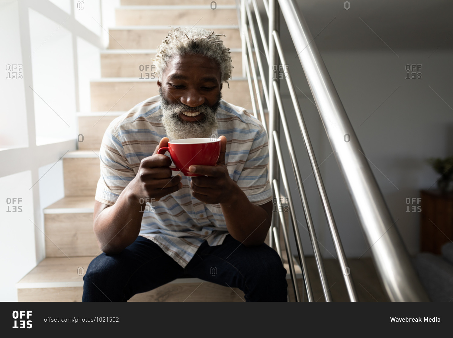 African American senior man sitting on stairs, holding a cup of coffee and smiling, social distancing and self isolation in quarantine lockdown