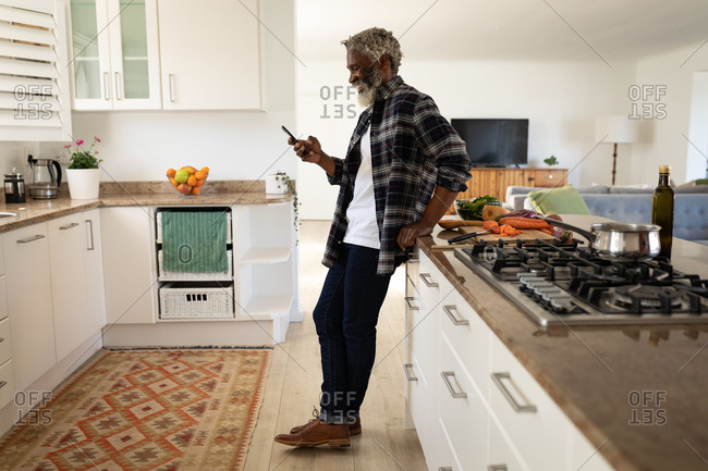 African American senior man standing in a kitchen, using a smartphone, social distancing and self isolation in quarantine lockdown