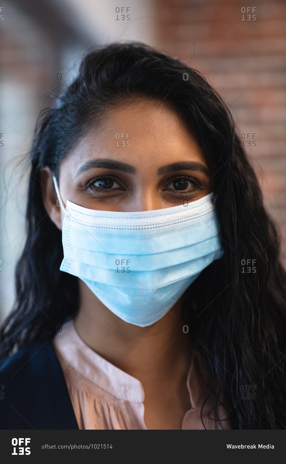 Portrait of mixed race woman working in a casual office, wearing face mask and looking at camera. Social distancing in the workplace during Coronavirus Covid 19 pandemic.