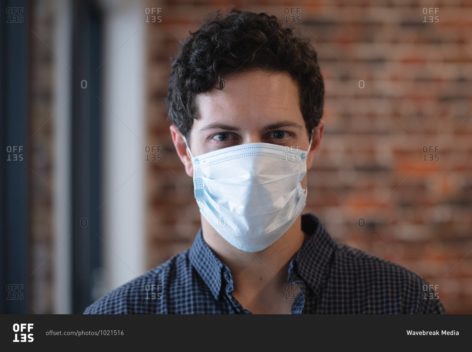Portrait of Caucasian man working in a casual office, wearing face mask and looking at camera. Social distancing in the workplace during Coronavirus Covid 19 pandemic.