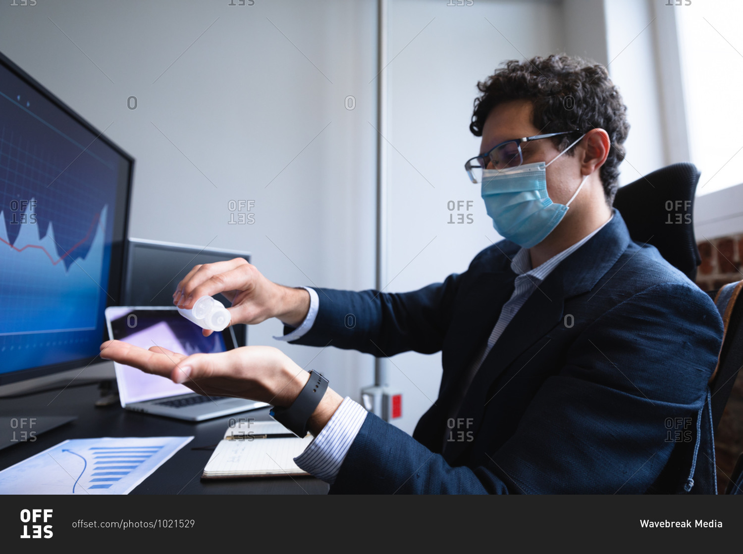 Caucasian man working in a casual office, using sanitizer and wearing face mask. Social distancing in the workplace during Coronavirus Covid 19 pandemic.