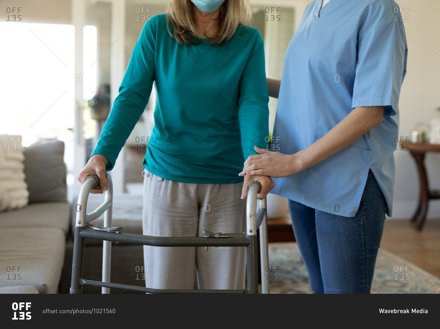 Senior Caucasian woman at home visited by Caucasian female nurse, walking using a walker, wearing face mask. Medical care at home during Covid 19 Coronavirus quarantine.