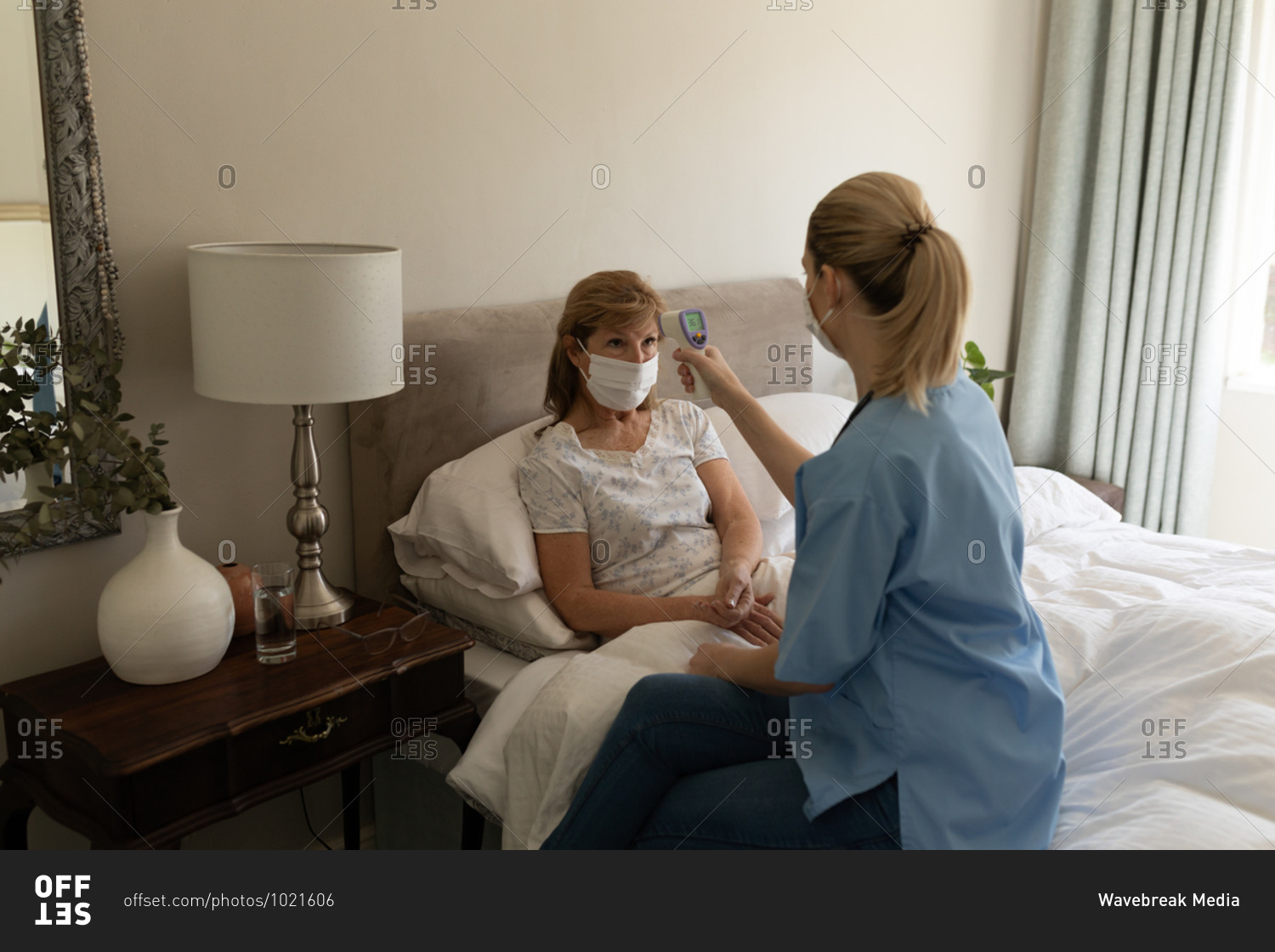 Senior Caucasian woman at home visited by Caucasian female nurse, checking temperature. Medical care at home during Covid 19 Coronavirus quarantine.