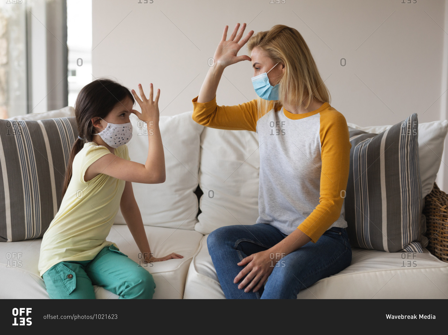 Caucasian woman and her daughter spending time at home together, wearing face masks, having a conversation using sign language. Social distancing during Covid 19 Coronavirus quarantine lockdown.