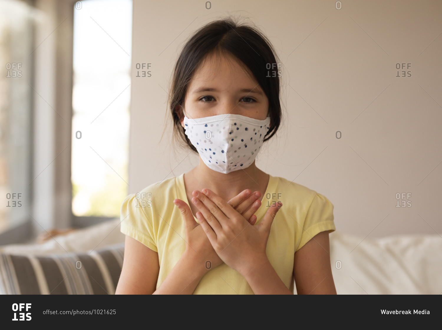 Portrait of Caucasian girl spending time at home, wearing face mask, looking at camera, using sign language. Social distancing during Covid 19 Coronavirus quarantine lockdown.