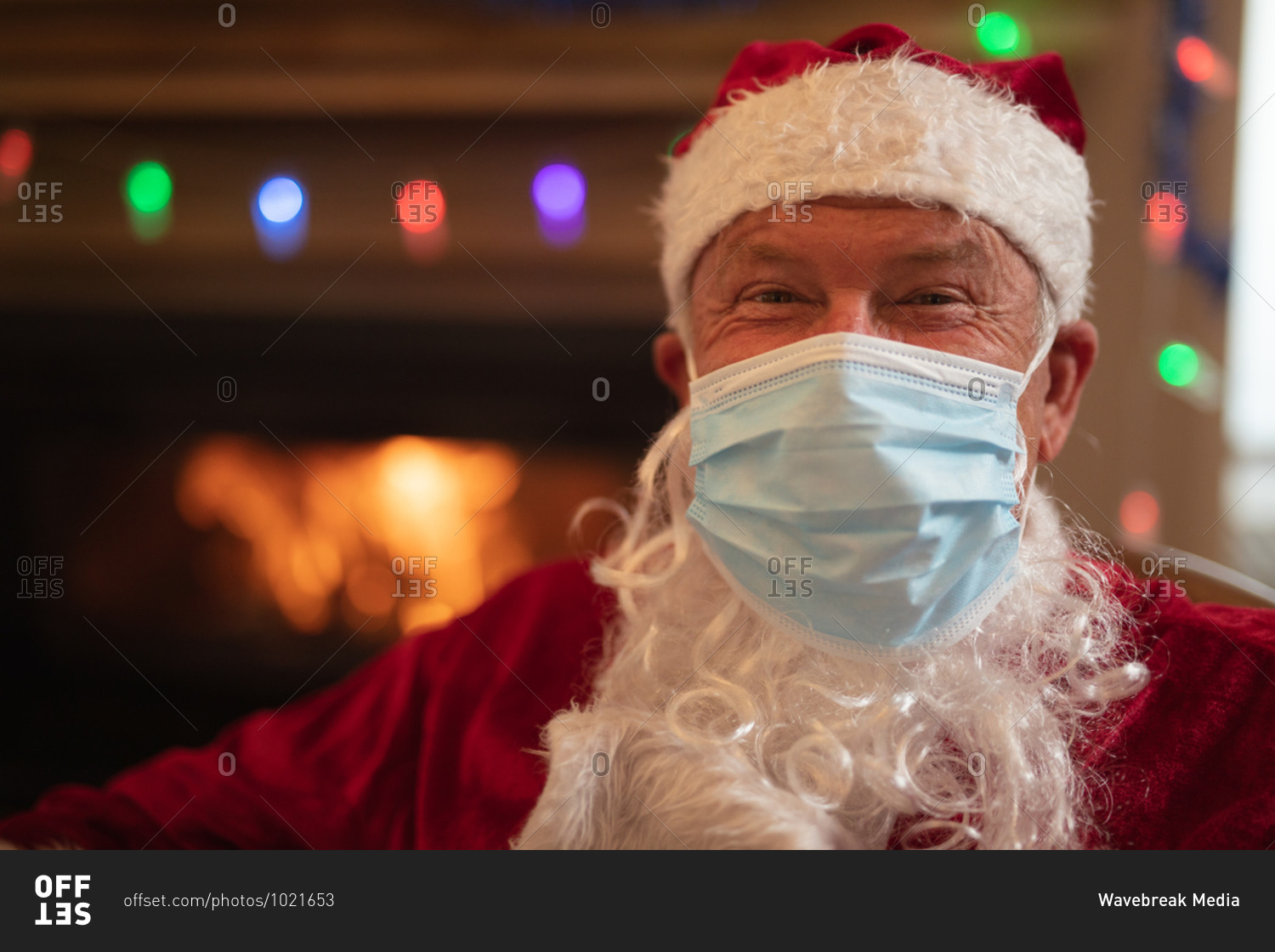 Portrait of senior Caucasian man at home dressed as Father Christmas, wearing face mask, looking at camera. Social distancing during Covid 19 Coronavirus quarantine lockdown.