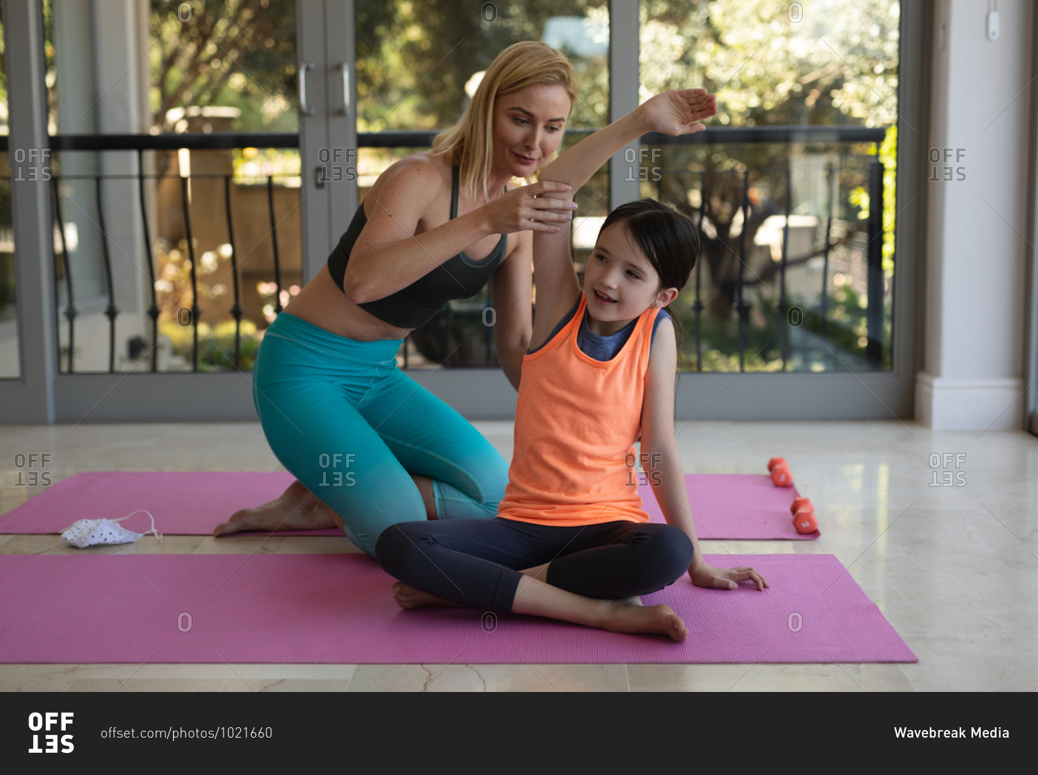 Caucasian woman and her daughter spending time at home together, doing yoga, stretching. Social distancing during Covid 19 Coronavirus quarantine lockdown.