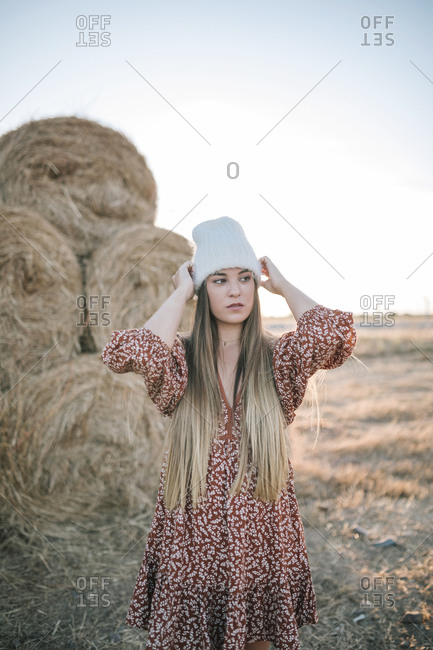 Portrait of young woman with woolen hat in front of a pile of straw in the field