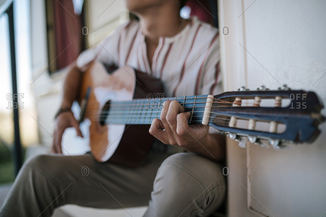 Young teenage man playing guitar sitting in the doorway of a caravan