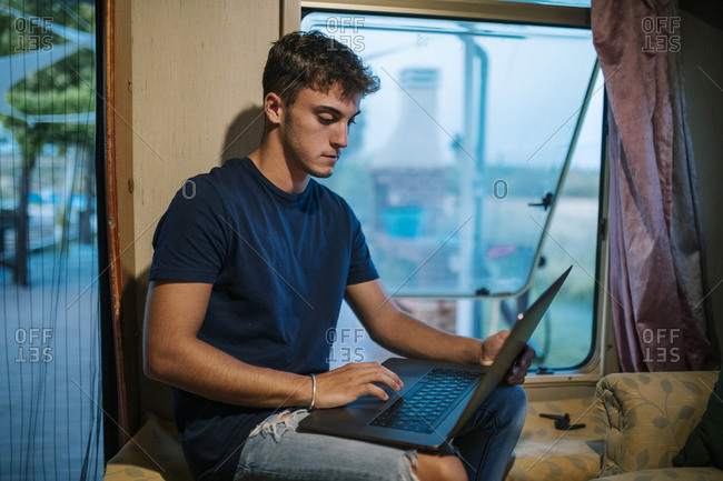 Young man with laptop inside a caravan