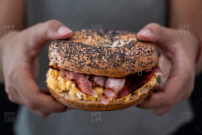 Women's hands holding a bagel with bacon and egg