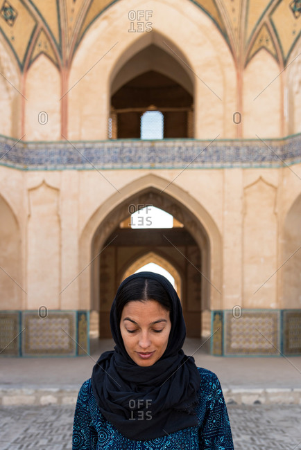 Ethnic woman in traditional clothes standing at Middle Eastern building with arch in Khasan, Iran.