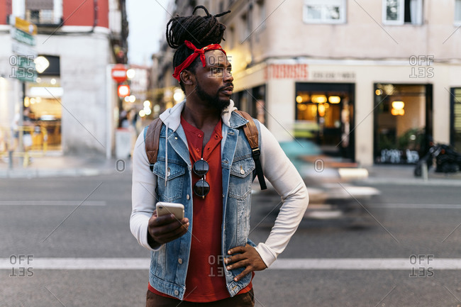 Attractive African American man with dreadlocks and a bandana walking in the street and using his phone