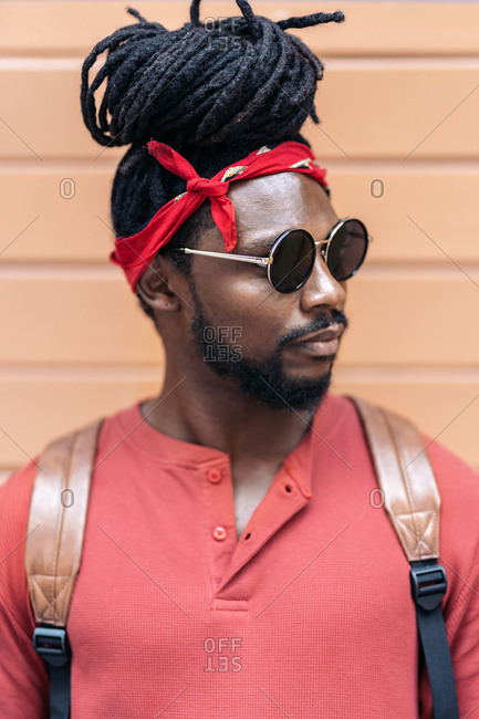African American man with dreadlocks looking away in front of orange background